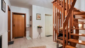 A hallway with a wooden staircase, a door, a small table with flowers, and a framed picture on the wall. - Cozy apartment in Goslar OT Hahnenklee with WiFi (Goslar OT Hahnenklee)