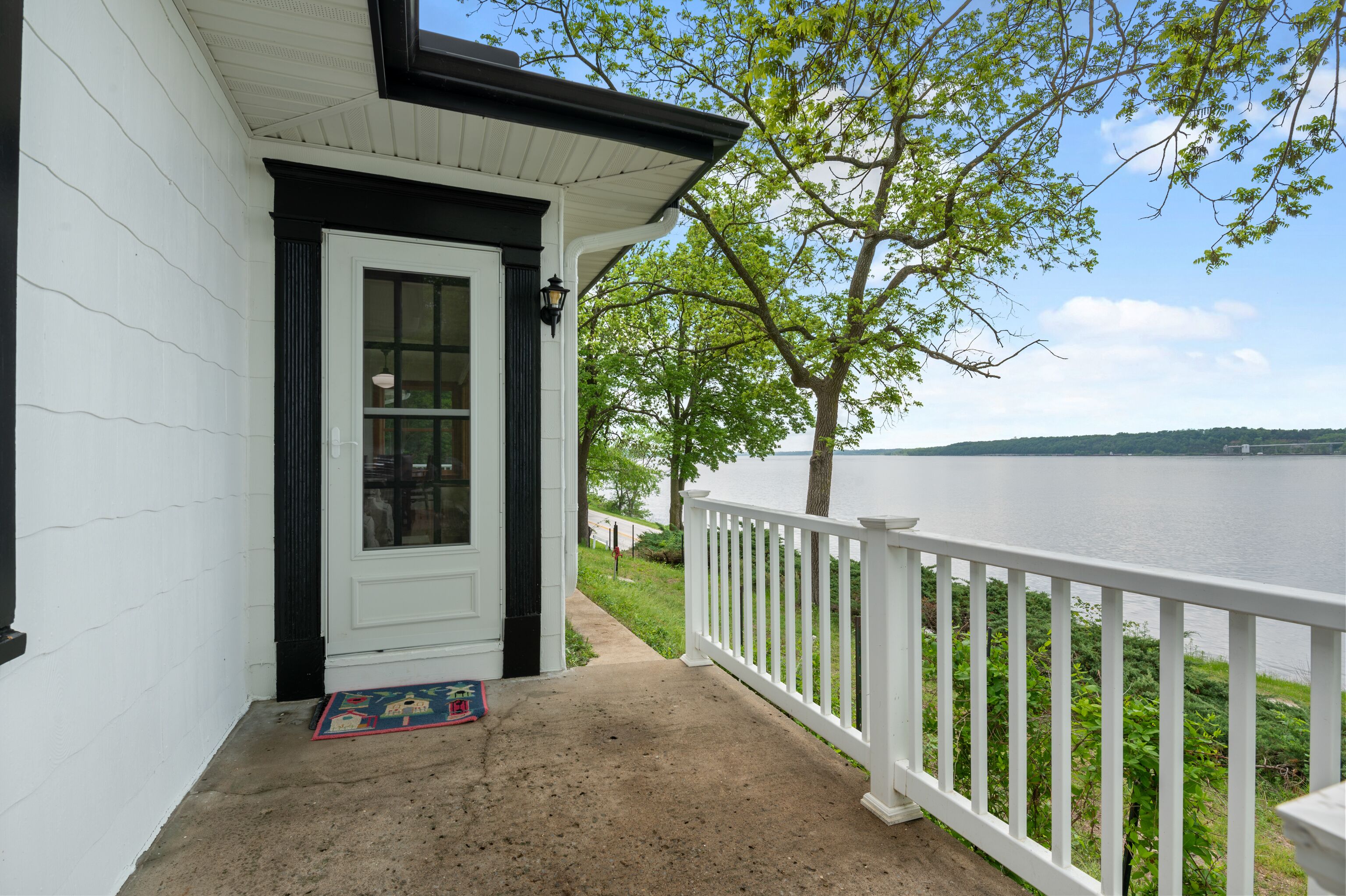 A white building with a black door and a white railing overlooking a body of water.