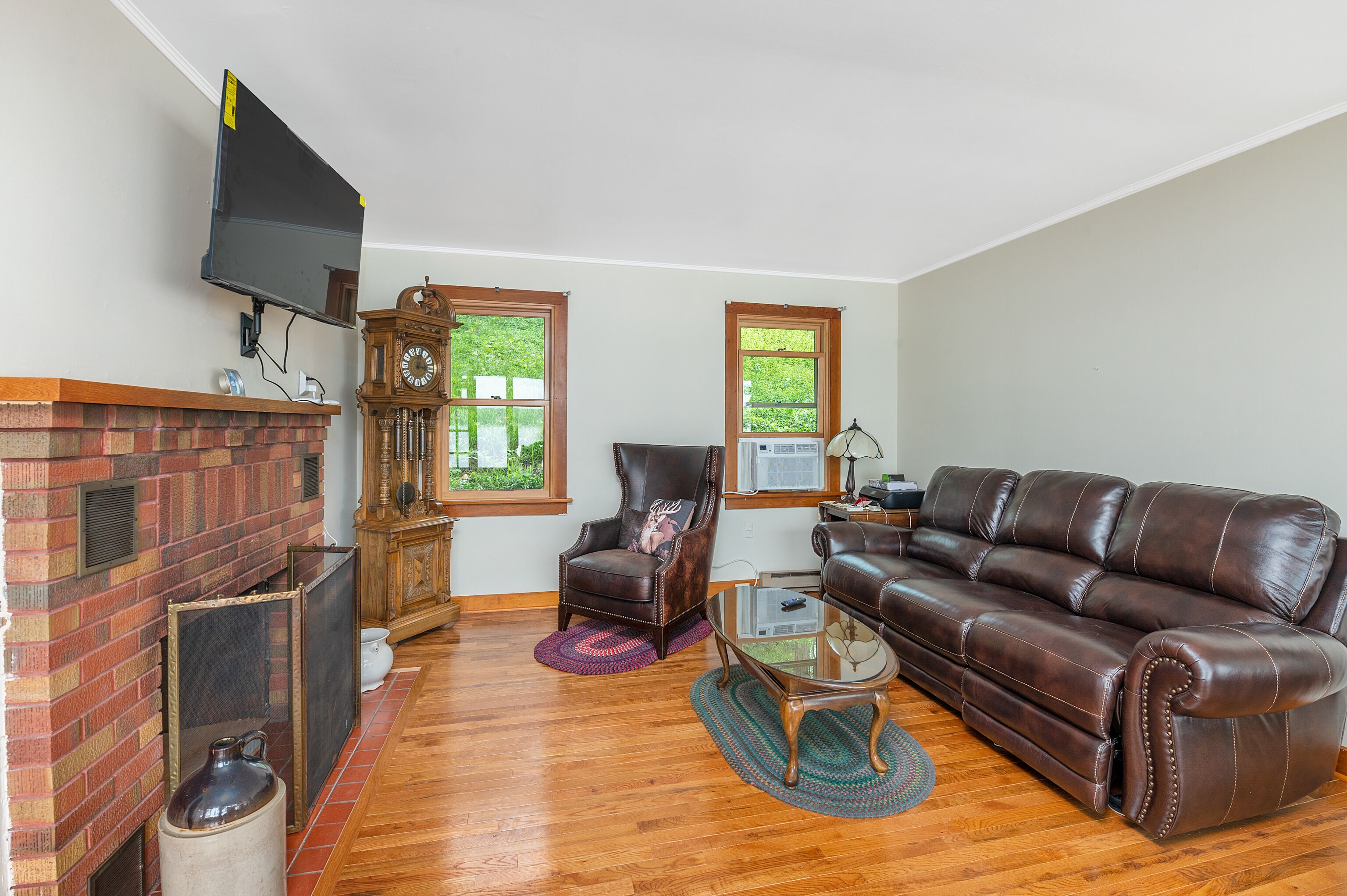A living room with a brick fireplace, leather sofa, and a television mounted on the wall.