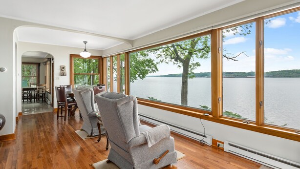 A spacious room with large windows offering a view of a lake and trees. There are two gray armchairs and a dining table with chairs.