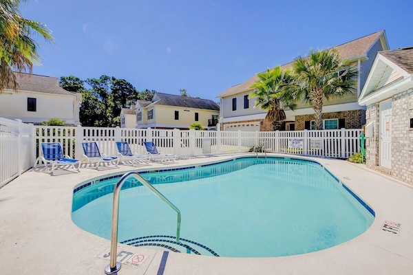 Inviting pool with lounge chairs, palm trees, and a white picket fence.