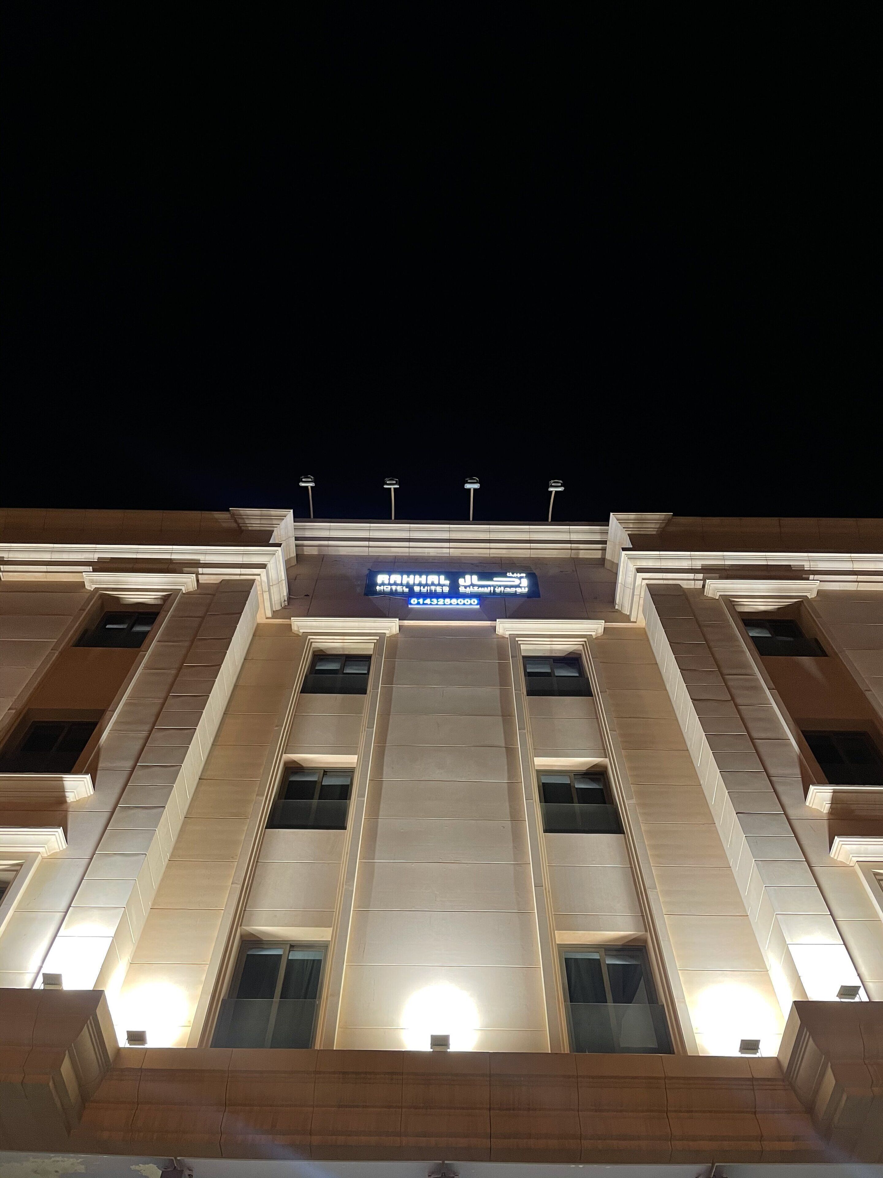 A hotel facade with a large illuminated sign displaying the name and contact number.