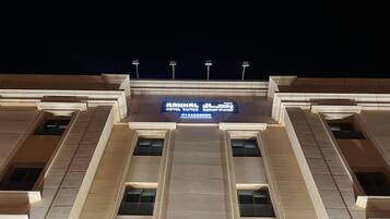 A hotel facade with a large illuminated sign displaying the name and contact number.