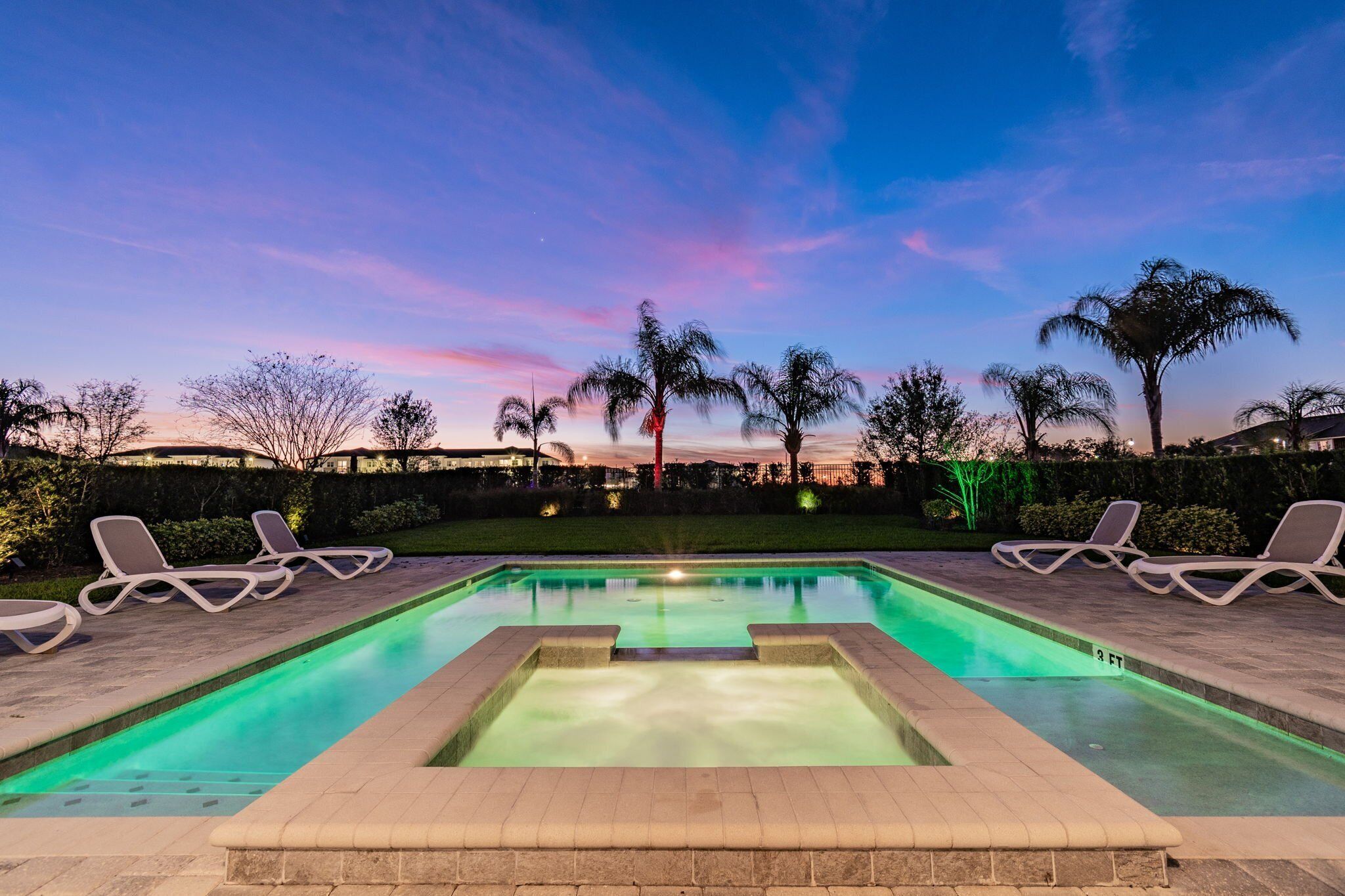 A swimming pool with lounge chairs and a sunset view.