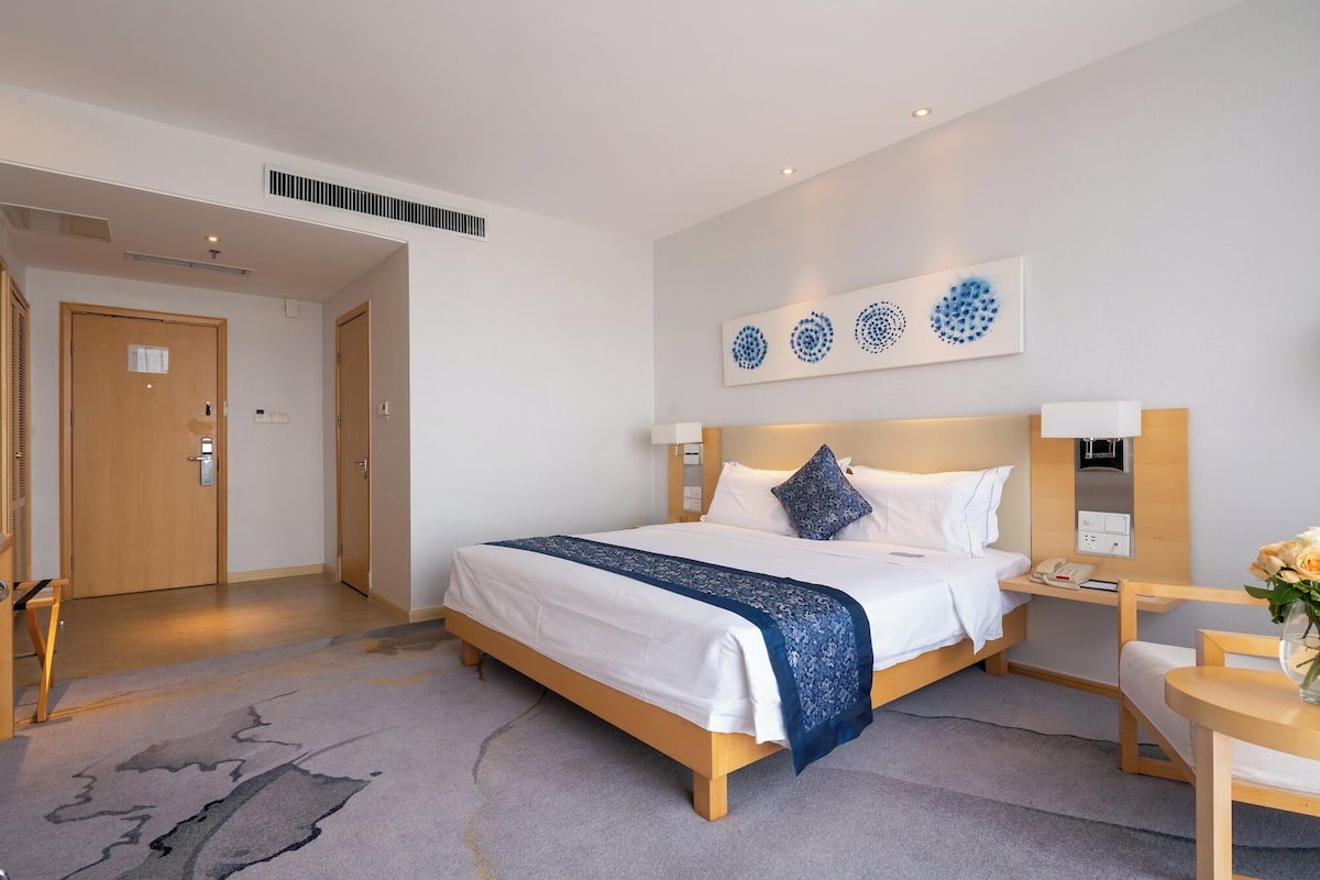 Une chambre d’hôtel avec un lit, une table de chevet, une lampe et un vase de fleurs.