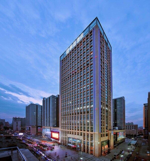 Un hotel de gran altura con un diseño moderno, que destaca una llamativa banda de luz vertical y un gran anuncio digital en la base.