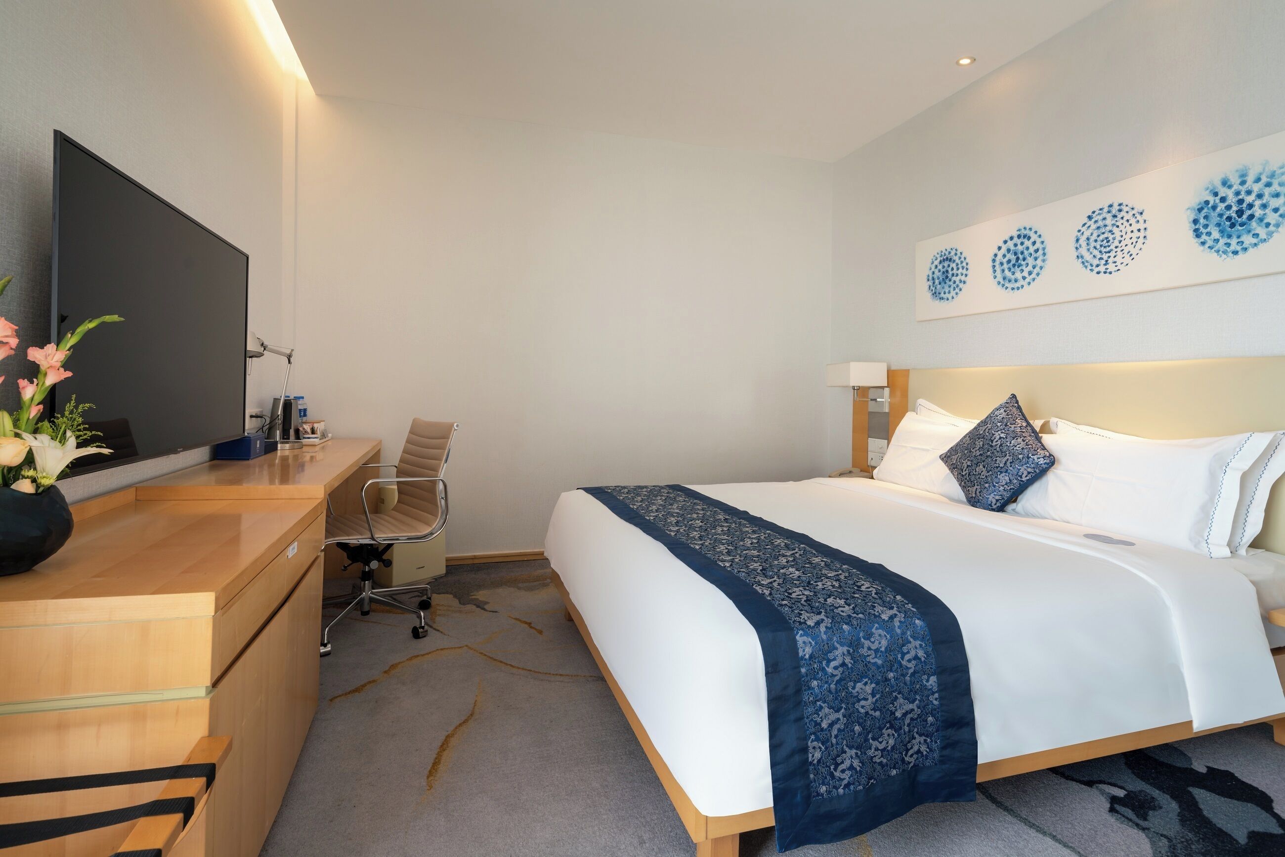 Habitació d'hotel amb llit, escriptori, cadira, televisió i obra d'art a la paret.