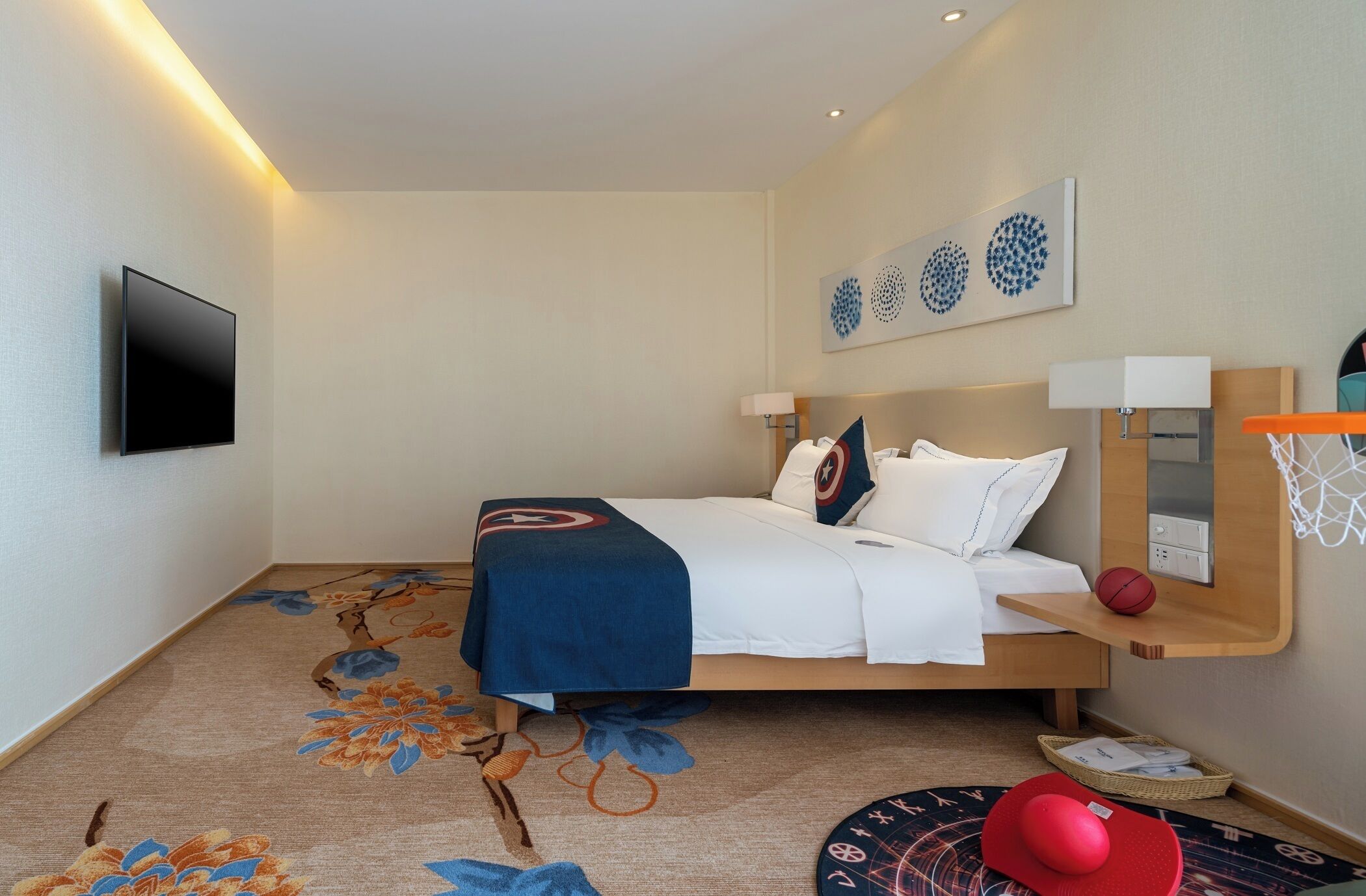 Quarto de hotel com cama, televisão de tela plana, prateleira na parede com uma bola de basquete e tapete decorativo.