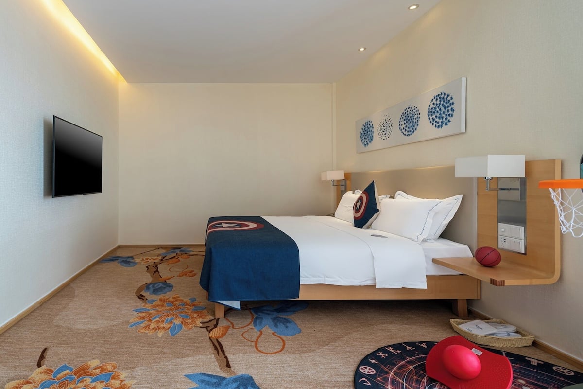 Une chambre d’hôtel comprenant un lit, un téléviseur à écran plat, une étagère murale avec un ballon de basket et un tapis décoratif.