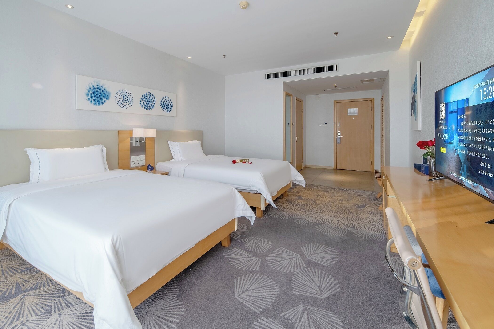 A hotel room with two beds, a TV, and a wooden desk.