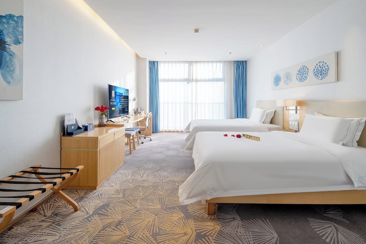 Une chambre d’hôtel avec deux lits, un bureau, une télévision et une vue sur l’extérieur.