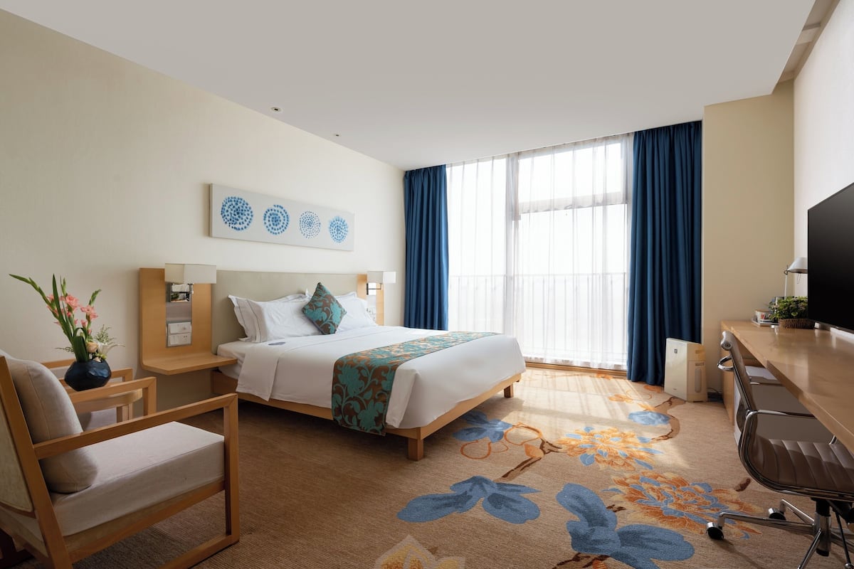 Une chambre d’hôtel équipée d’un lit, d’un bureau, d’une chaise, d’une télévision et d’une fenêtre avec des rideaux.