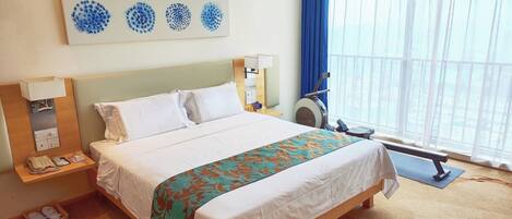 Una habitación de hotel con una cama, un escritorio con teléfono, una lámpara, una ventana con cortinas y un cuadro en la pared.