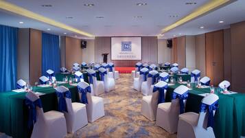 Sala de conferências com fileiras de cadeiras brancas com fitas azuis, mesas com garrafas de água e uma tela exibindo o logotipo do Novion Hotel.