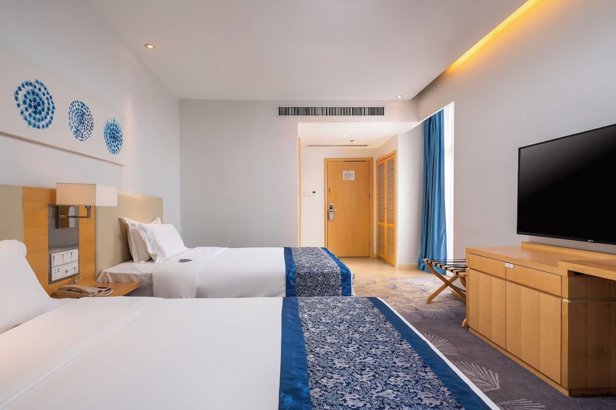 Une chambre d’hôtel avec deux lits, une télévision, un bureau et une salle de bain visible à travers une porte ouverte.