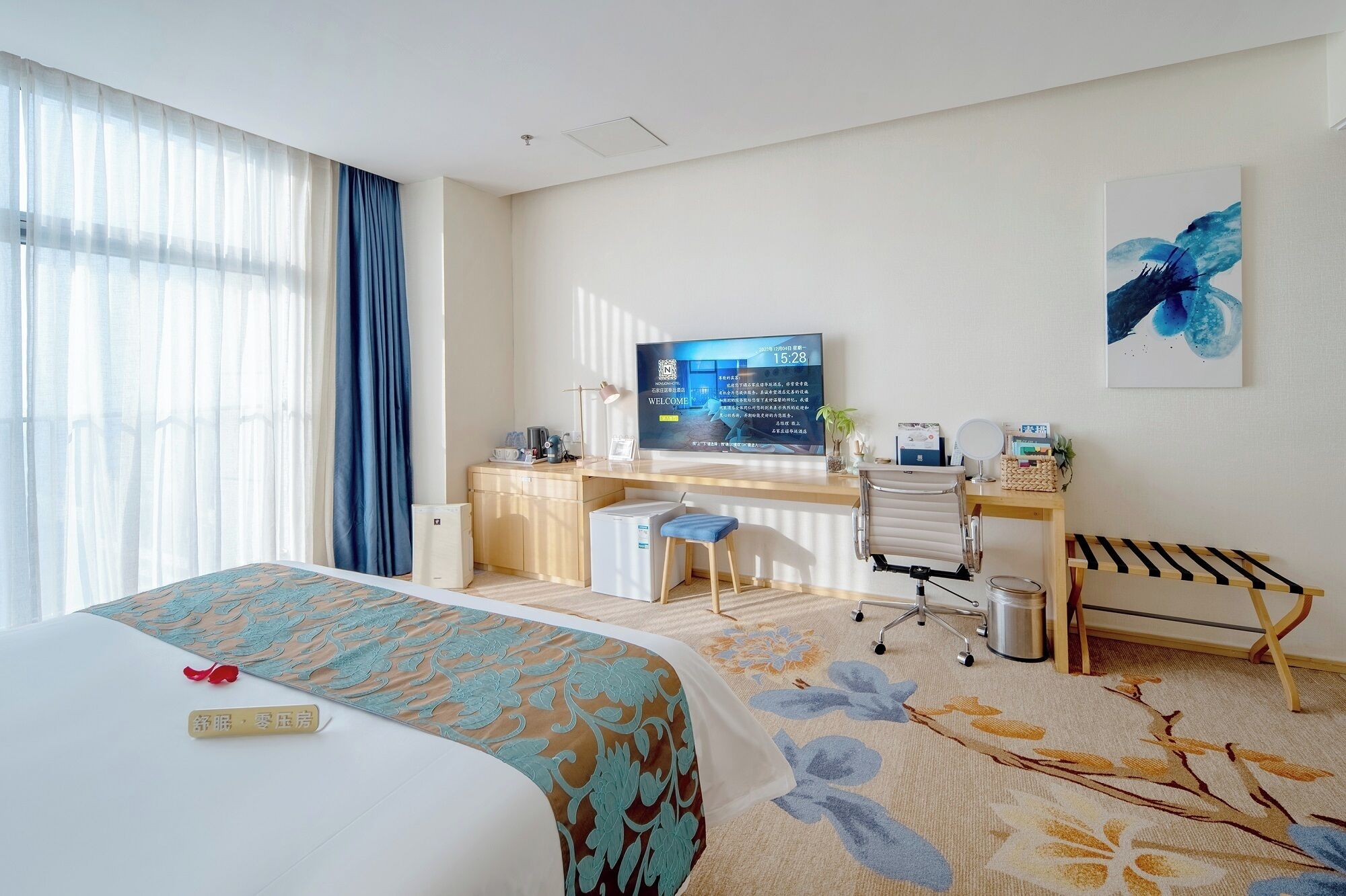 Een hotelkamer met een bed, bureau, stoel en een televisie waarop een welkomstboodschap staat.