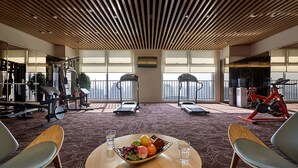 A gym with treadmills, stationary bikes, and weight machines. There is a table with a fruit bowl and glasses. - Shijiazhuang Nuohuating Hotel (Shijiazhuang)