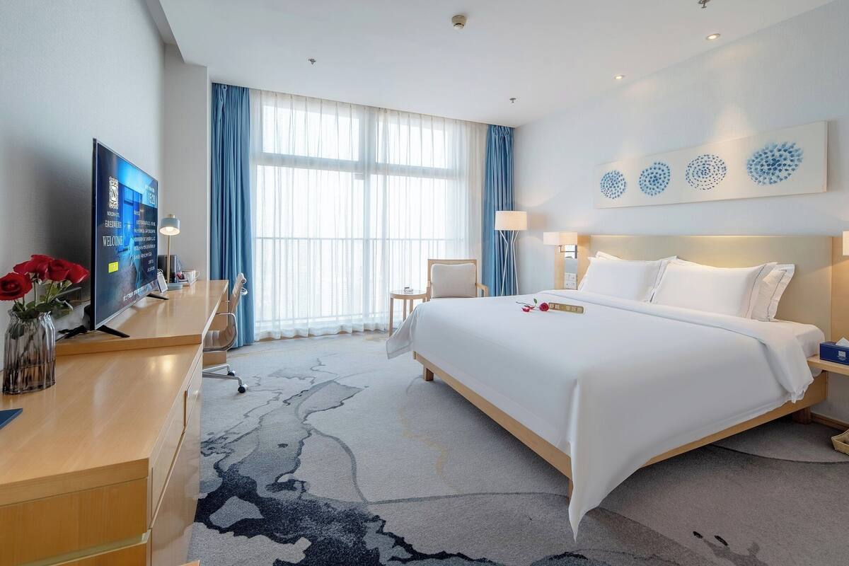 Une chambre d’hôtel avec un grand lit, un bureau, une télévision et une fenêtre avec des rideaux.