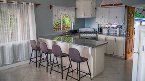 A kitchen with a central island, bar stools, a stove, and a refrigerator. - Majestic Villa, breathtaking view of famous Pitons, Ocean and Soufriere Town (Soufriere)