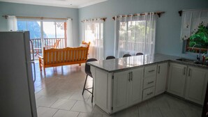 A kitchen with a central island, white cabinets, and a dining area with a wooden bench and chairs. - Majestic Villa, breathtaking view of famous Pitons, Ocean and Soufriere Town (Soufriere)