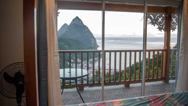 A balcony with a table and chairs, a fan, and a view of a mountain and ocean. - Majestic Villa, breathtaking view of famous Pitons, Ocean and Soufriere Town (Soufriere)