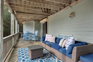 A covered porch with a wicker sofa, blue chairs, and a patterned rug. - Chase-n-Grace: Private Pool, Spacious Yard, Short Walk to Beach (Southern Shores)