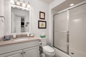 A bathroom with a sink, toilet, and shower. There are framed pictures on the wall.