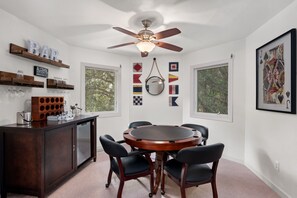 A dining area with a round table, chairs, a ceiling fan, and a bar area with shelves.