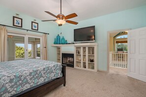 A bedroom with a bed, a TV, a ceiling fan, and a fireplace. - Chase-n-Grace: Private Pool, Spacious Yard, Short Walk to Beach (Southern Shores)