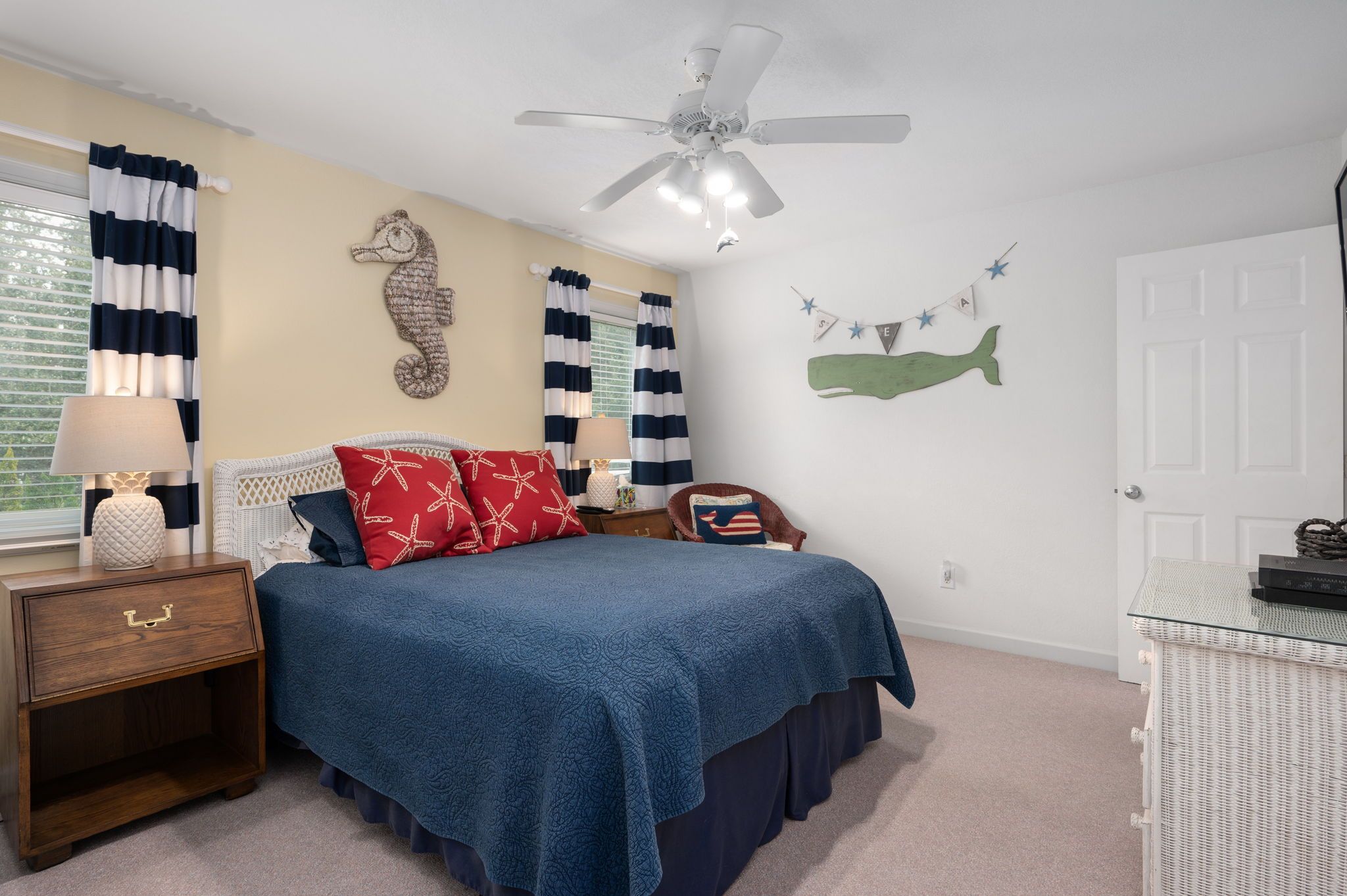 A bedroom with a bed, nightstands, a dresser, a ceiling fan, and nautical-themed wall decorations.