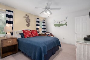 A bedroom with a bed, nightstands, a dresser, a ceiling fan, and nautical-themed wall decorations.