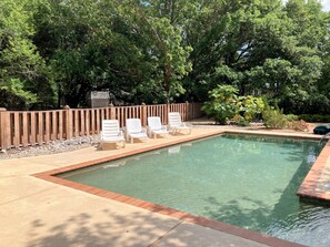 Ein Swimmingpool mit klarem Wasser, umgeben von einer Holzterrasse und einer Reihe weißer Liegestühle.