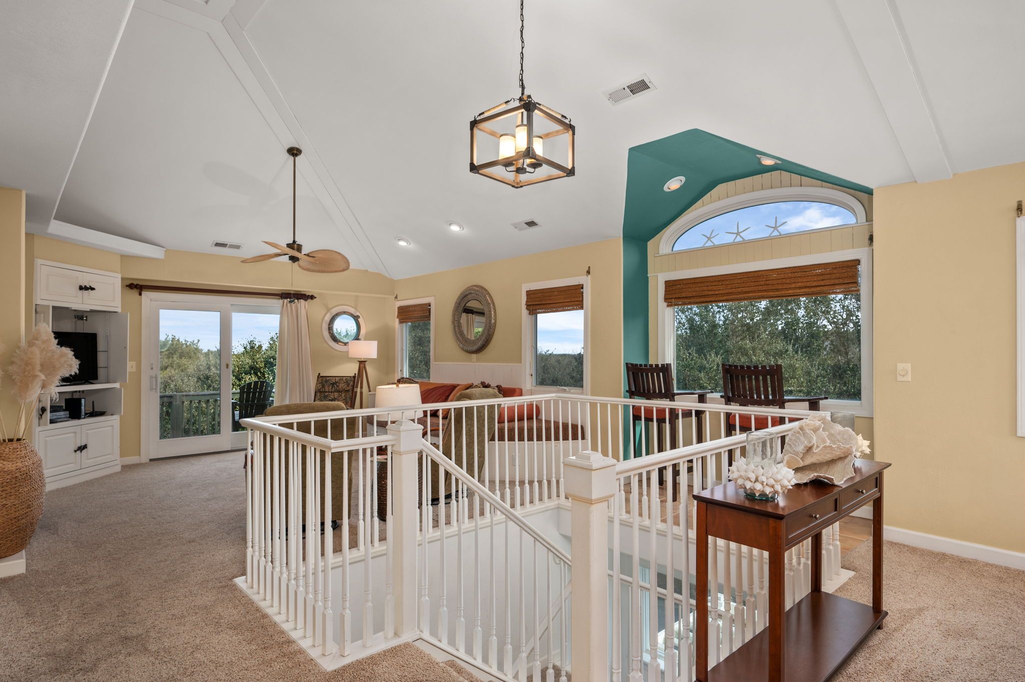 A spacious living area with a high ceiling, a ceiling fan, a large window with a view, and a staircase with a railing.