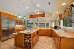A spacious kitchen with a central island, wooden cabinets, a stainless steel refrigerator, and pendant lighting.