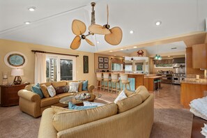A spacious living room with a large ceiling fan, a dining area with bar stools, and a kitchen with modern appliances.