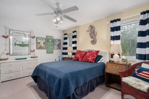 A bedroom with a bed, a nightstand, a chair, a ceiling fan, and wall decorations.