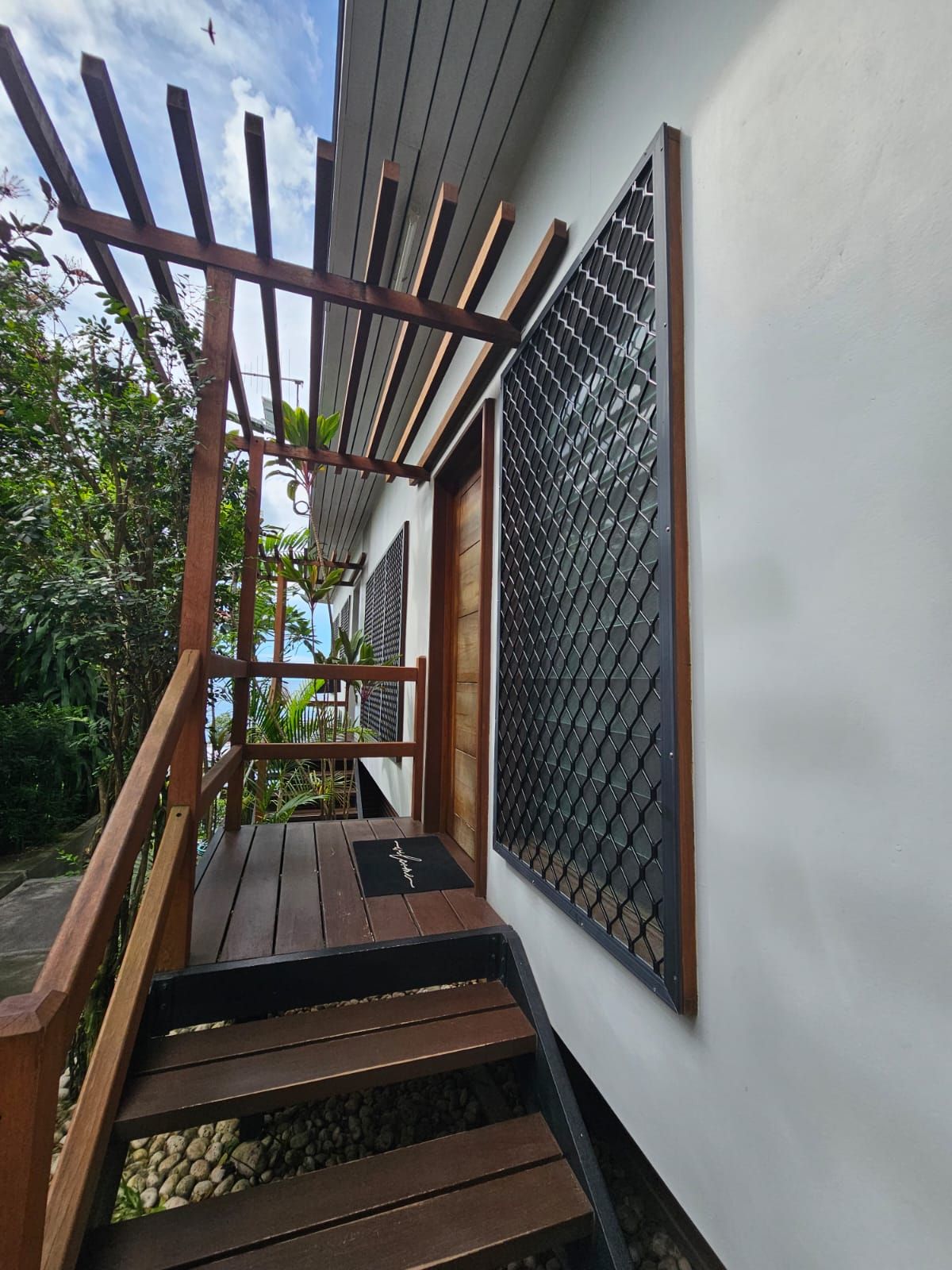 A wooden staircase leading to a door with a metal mesh panel.