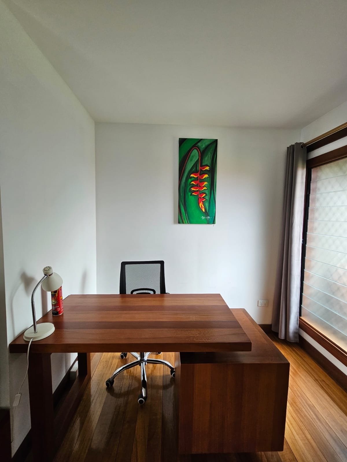 Quarto com escrivaninha de madeira, uma cadeira, abajur e um quadro na parede.