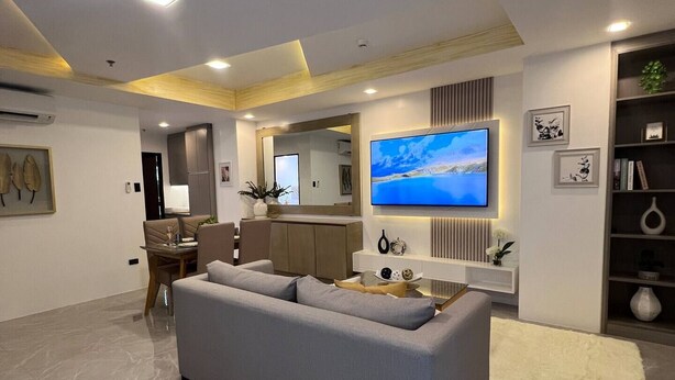 Ein modernes Wohnzimmer mit grauem Sofa, einem Flachbildfernseher und einem Essbereich mit Tisch und Stühlen.