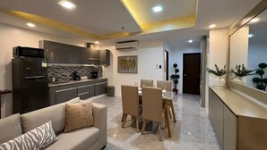 Ein modernes Wohnzimmer mit Sofa, Esstisch und Stühlen. Es gibt eine Küchenzeile mit Kühlschrank und Schränken.