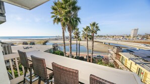 A balcony with wicker chairs overlooking a beach, a bridge, and a parking area with solar panels. - Luxury unit - Amazing Ocean & Harbor Views - Huge Kitchen - NCV G216 (Oceanside)