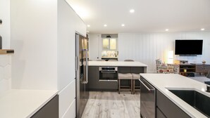 A modern kitchen with a central island, built-in appliances, and a flat-screen TV mounted on the wall. - Luxury unit - Amazing Ocean & Harbor Views - Huge Kitchen - NCV G216 (Oceanside)