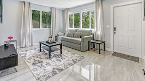 A modern living room with a grey sofa, two black side tables, a black coffee table, and a patterned rug. - Hallandale Collection: Renovated Professional Design & Lake View (Hallandale)