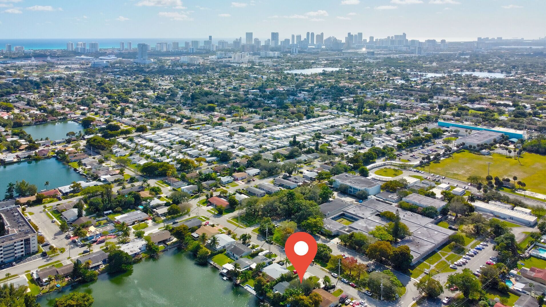 An aerial view of a residential area with a large body of water, a dense cluster of houses, and a distant city skyline.