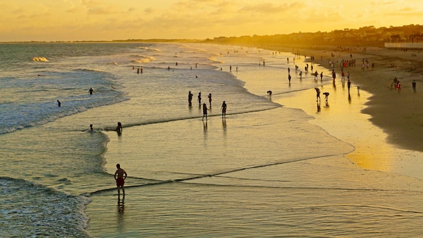 A beach scene with people walking along the shore and the ocean in the background.