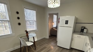 A modern kitchen with a white refrigerator, a dining table with chairs, and a pendant light.