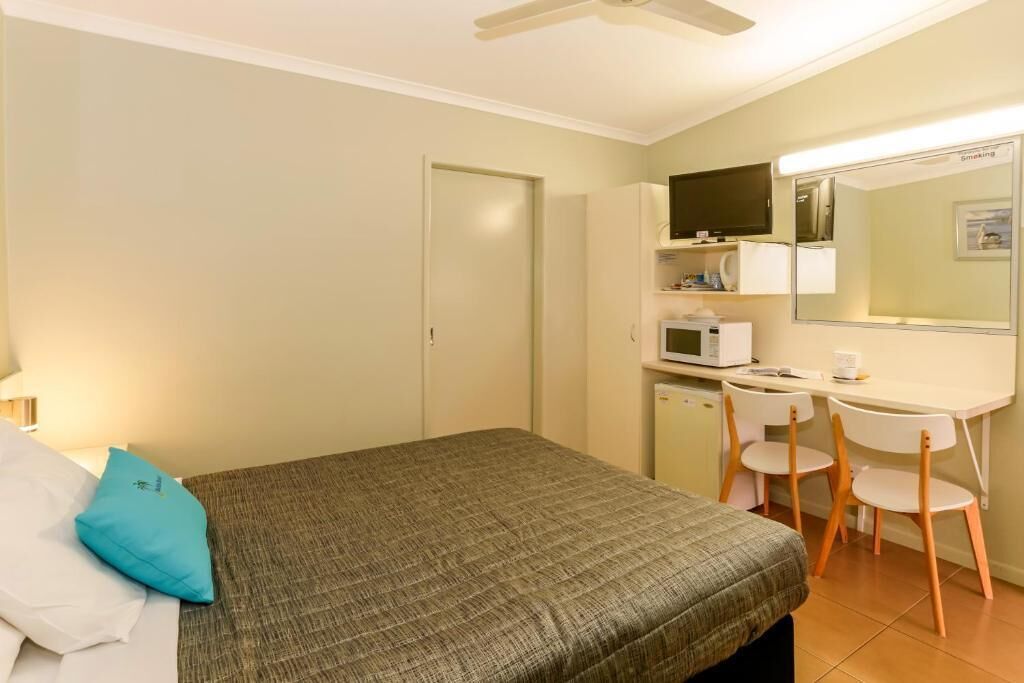 Habitación de hotel con cama, escritorio con silla, televisor, microondas y espejo.