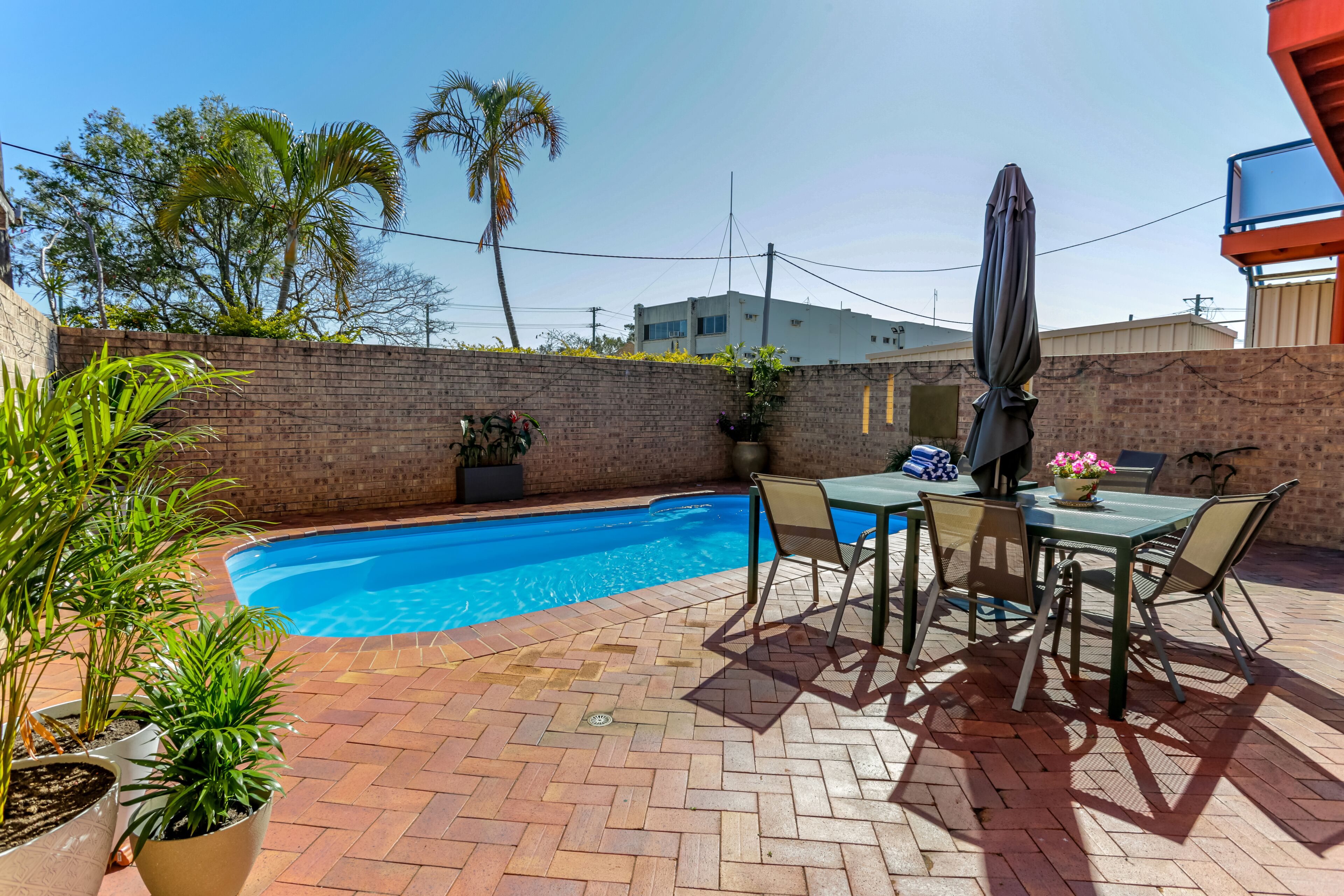 Piscina com um terraço de tijolos, área de estar ao ar livre e vasos de plantas.