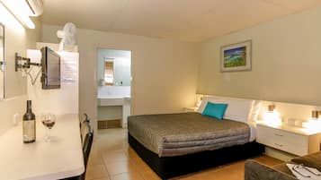 A hotel room with a bed, bedside table, chair, and a desk with a chair. There is a bottle and glasses on the desk.