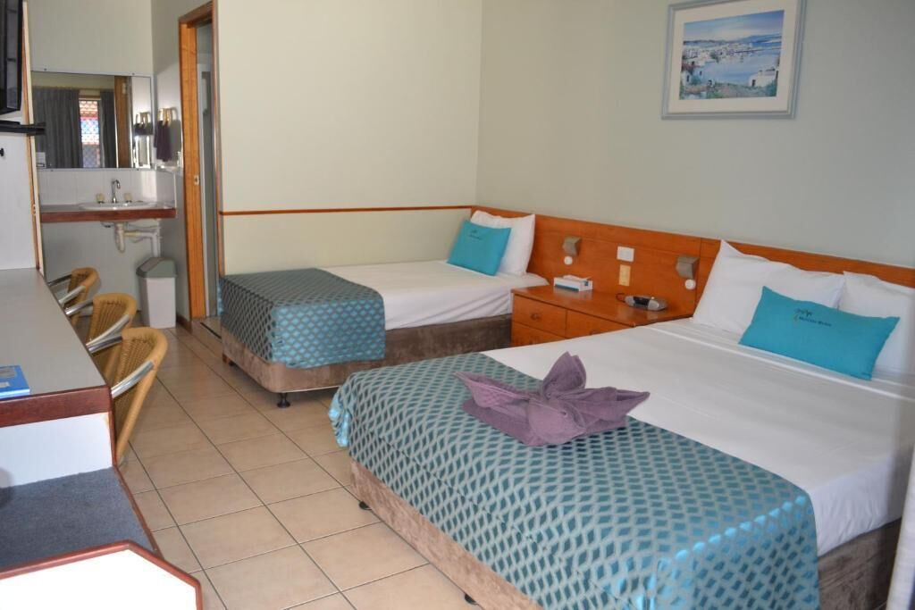 A hotel room with two beds, a desk, a chair, and a bathroom.